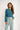 Woman wearing a teal top and light blue pants on a white background