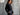 Woman in a black outfit standing against a textured gray wall with white clouds.